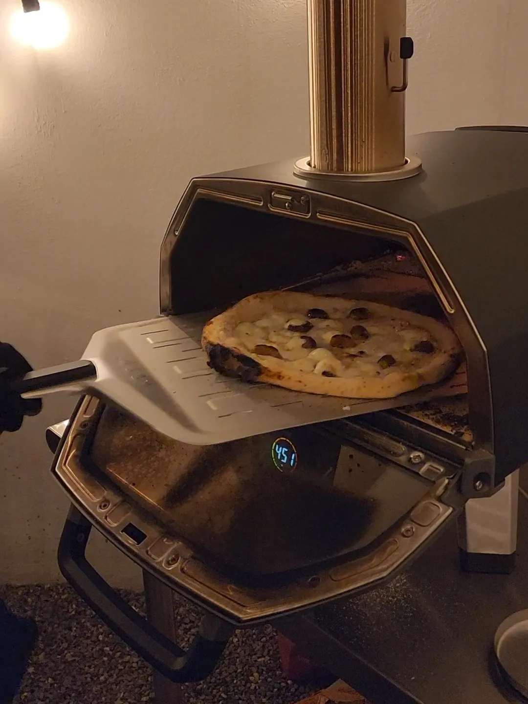 Pizza blanca saliendo del Ooni en la pala perforada, de noche
