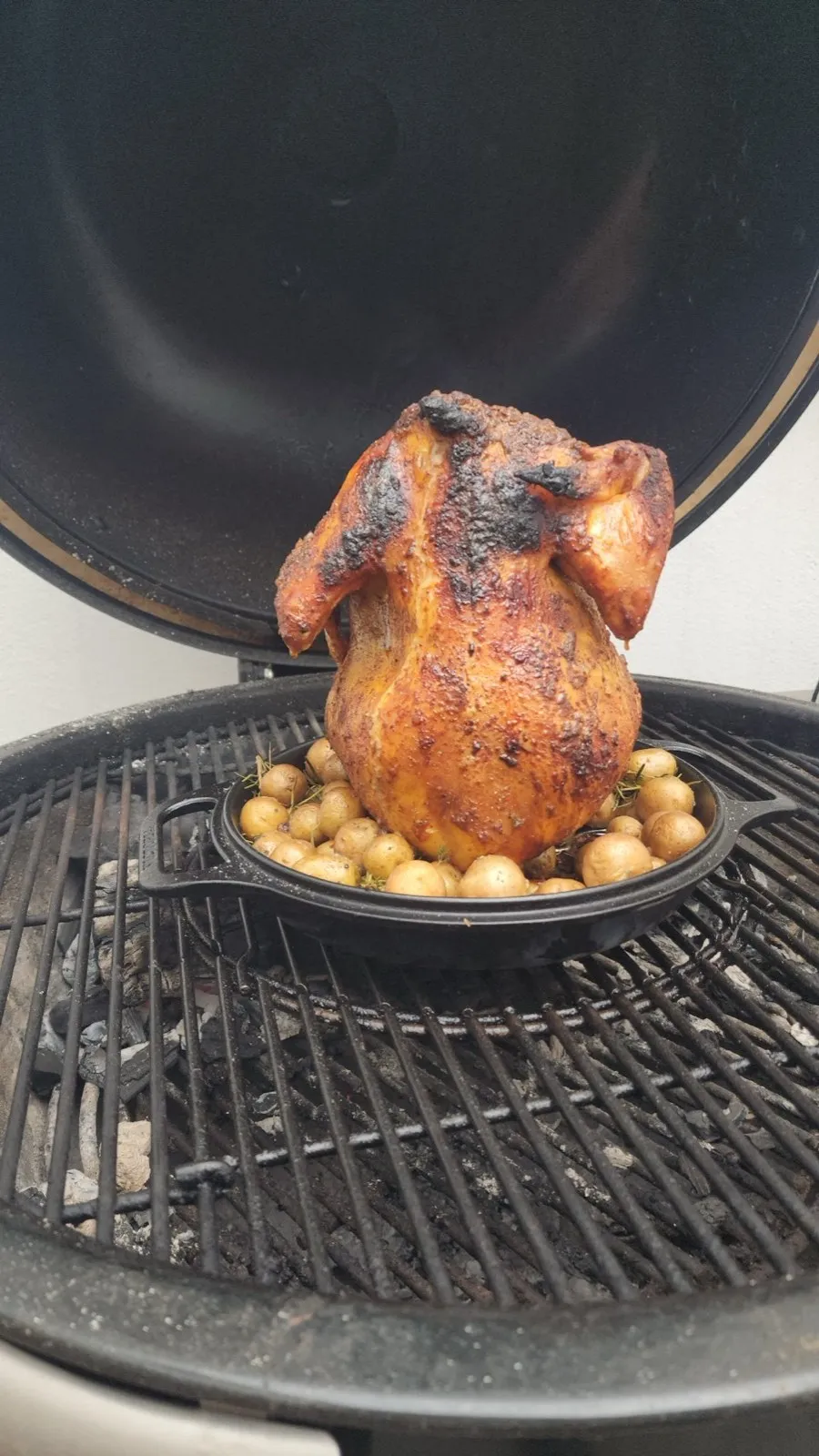 Pollo dorado sentado en el accesorio de hierro dentro del Kamado, con papas abajo