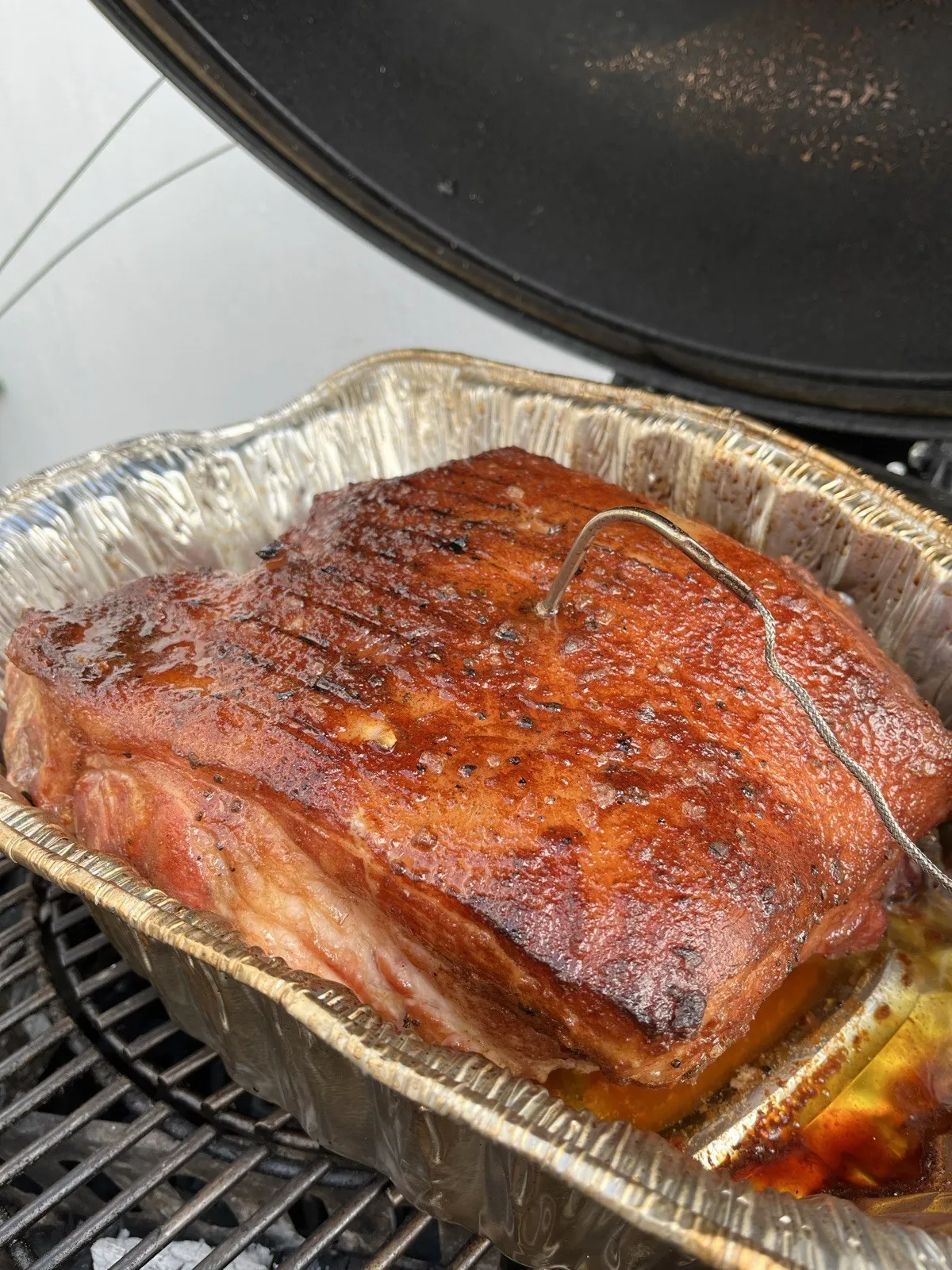 Paleta de cerdo con costra oscura en una charola de aluminio dentro del Kamado